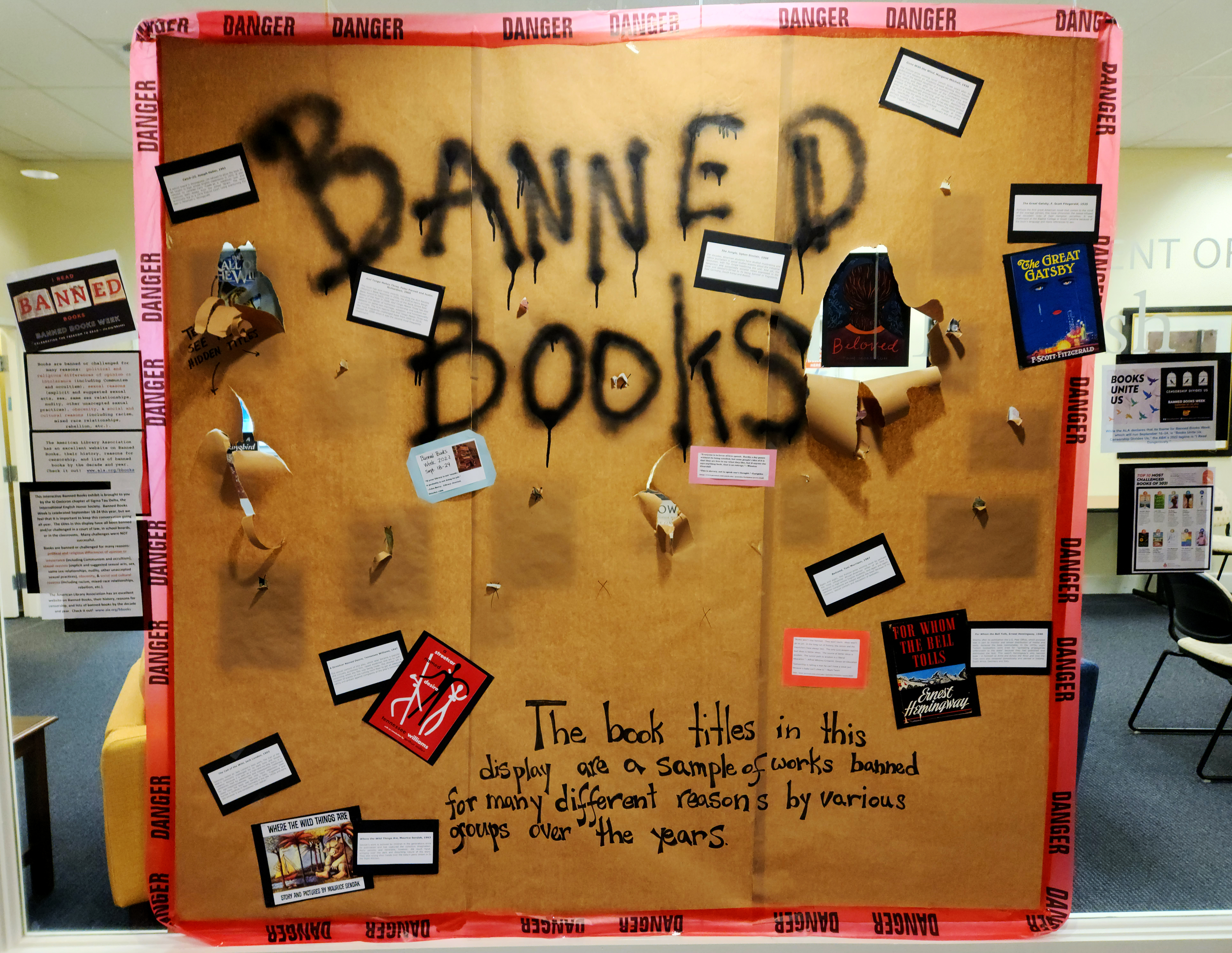 A window display surrounded by warning tape at the English department office invites passersby to tear the paper and reveal the covers of banned books.