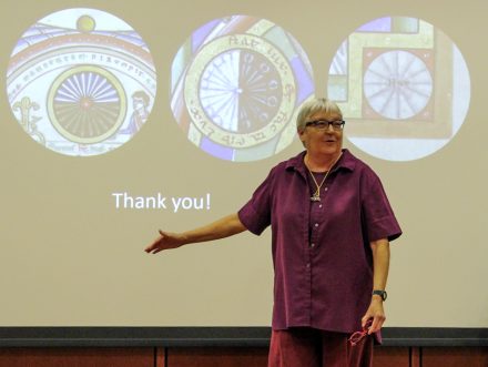 Elizabeth C. Teviotdale stands in front of a projected image of three circular illustrations of time reproduced from the Stammheim Missal.