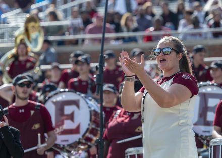 Poff clapping with the marching band behind her in the stadium