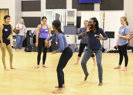 A group of high school-aged dancers stand in a circle around a professor and student performing a dance inside Scott Studios.