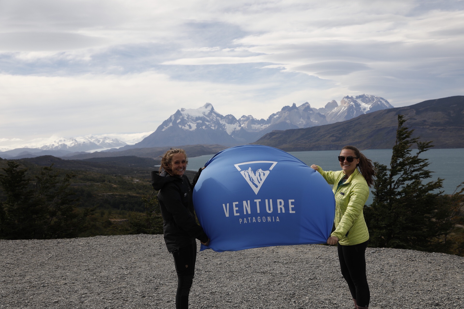 Carrie MacLean '16 (left) with Katie Zell Kelley ’03 (right) holding a Venture Patagonia flag in front of the peaks.