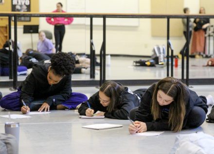 Three students lie on the floor of a dance studio while writing