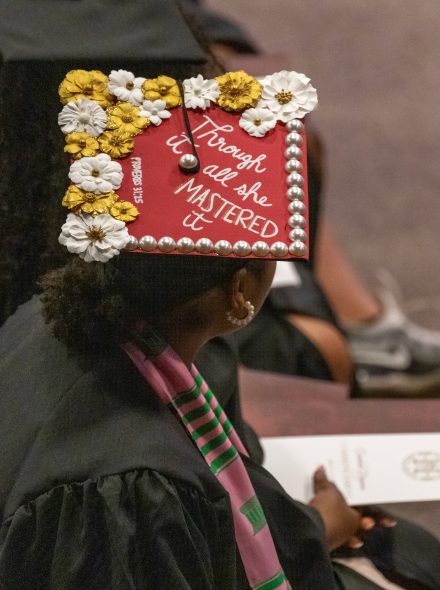 A master's-level graduate with a mortarboard that reads "Through it all, she mastered it"