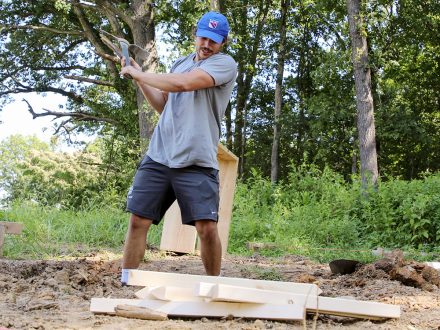 A student in front of piled lumber using a pick axe