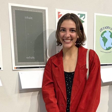 Young woman stands with award-winning poster at graphic design event.