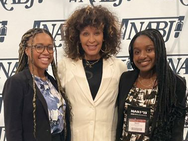 Three Black women stand before an NABJ backdrop.