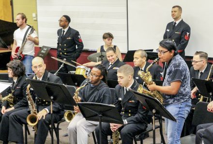 A group of students and naval officers playing instruments in a band room