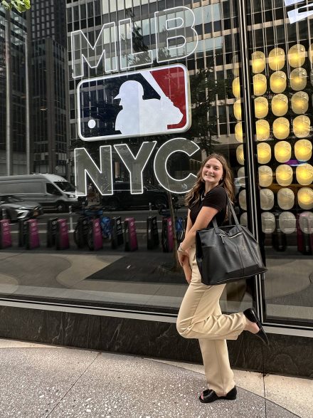 Cappellett smiles in front of an MLB sign that hangs on a glass wall.