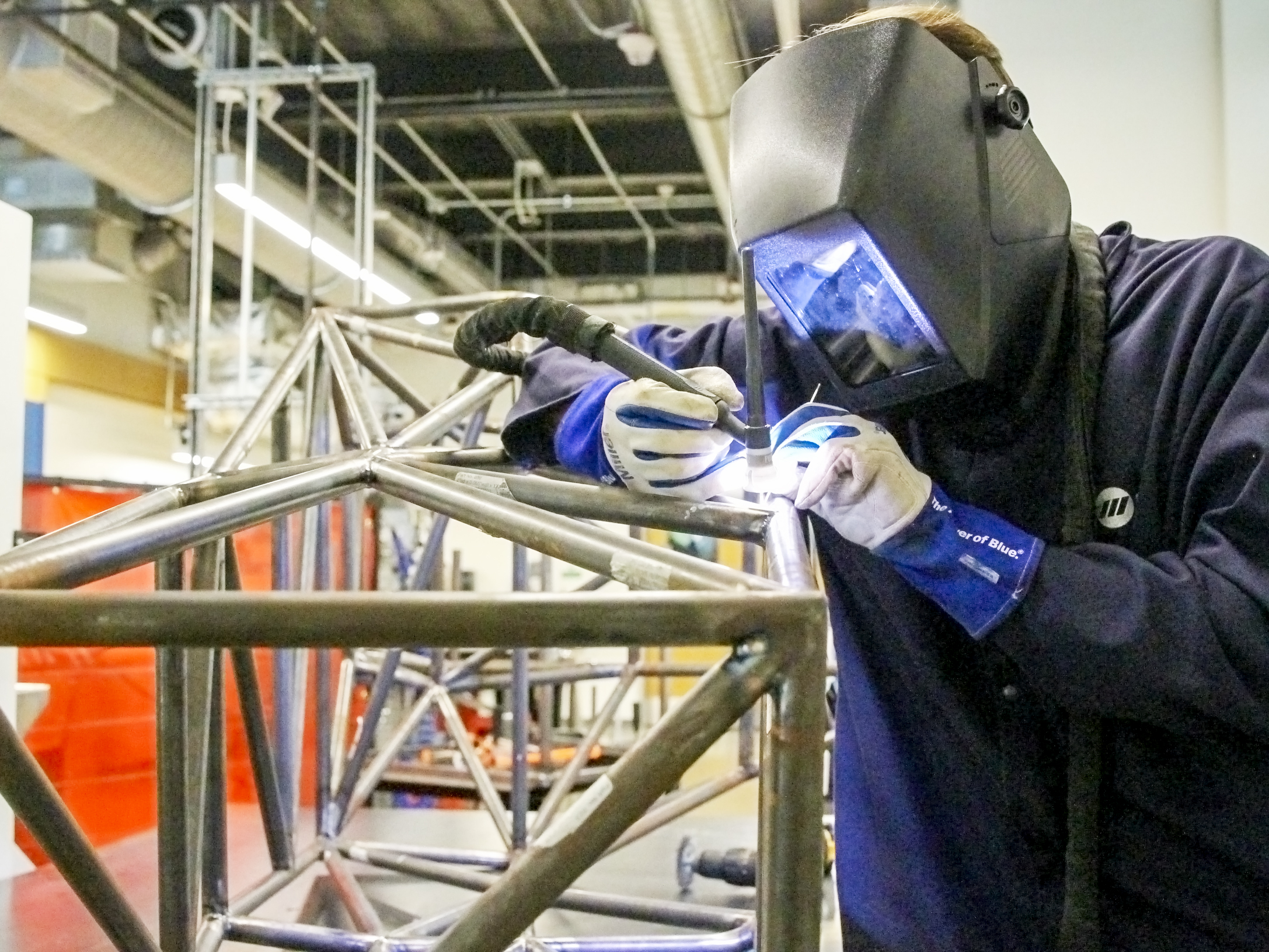 A student in a welding mask and gloves welding a car frame