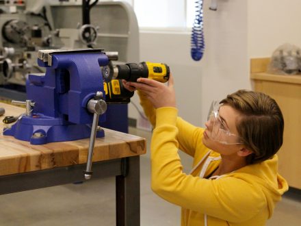 A female student using a rotary tool to smooth edges of a metal part