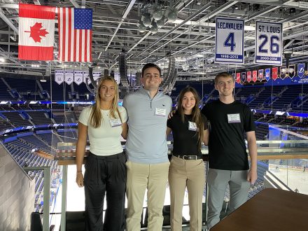 Four students post with a hockey arena in the background.