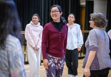 A professor encircled by students in a dance studio