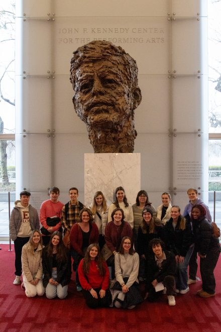 A group posed in front of a large bust of President John. F. Kennedy