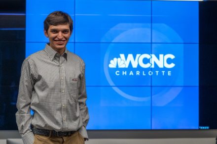 Elon alumnus Jack Norcross stands in front of a WCNC Charlotte screen.