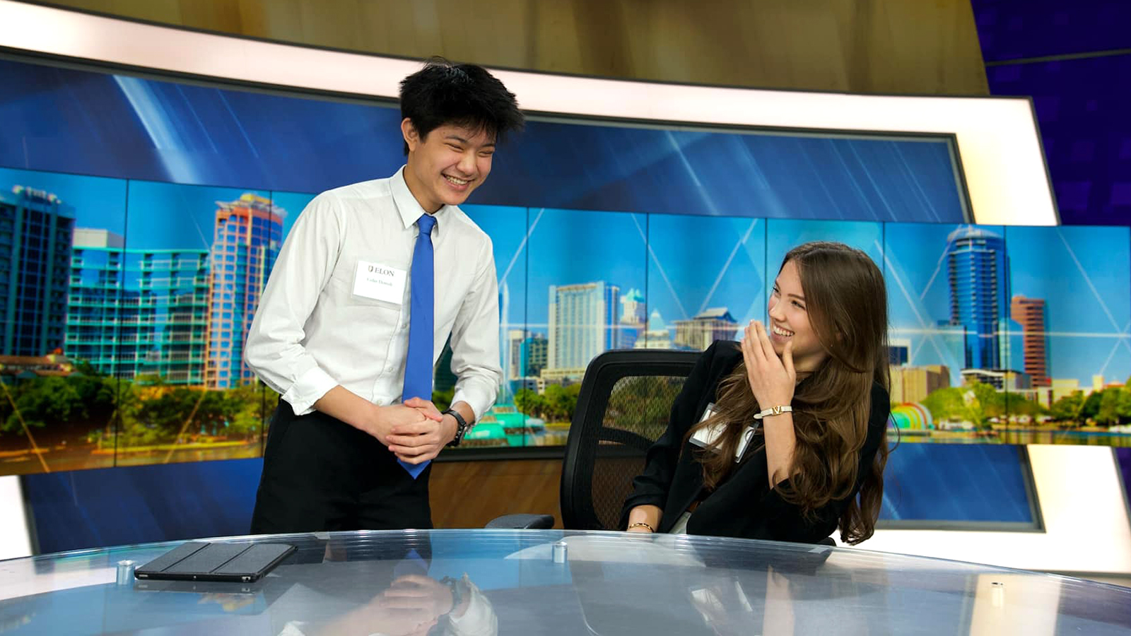 Two Elon School of Communications laugh at an anchor desk in Orlando, Florida.