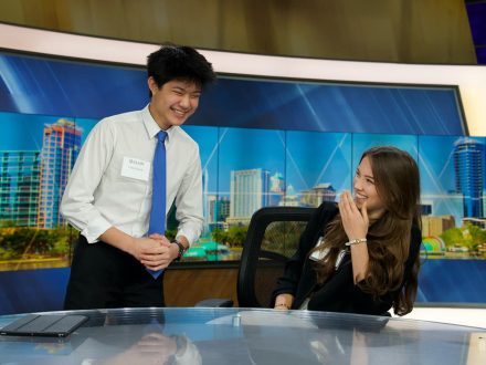 Two Elon School of Communications laugh at an anchor desk in Orlando, Florida.
