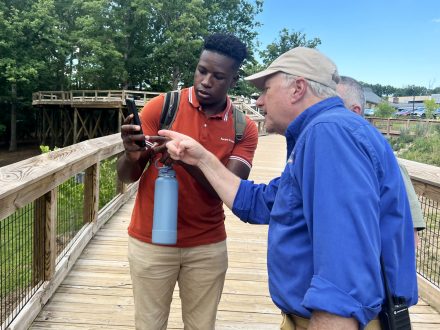 Two men looking at a phone screen on an outdoor boardwalk