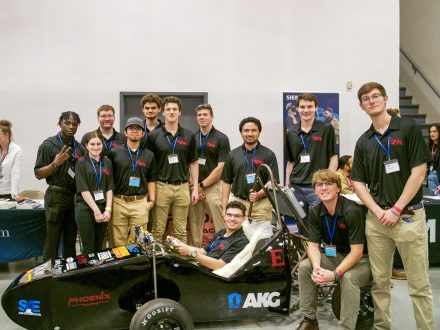 11 students posed by a black electric race car