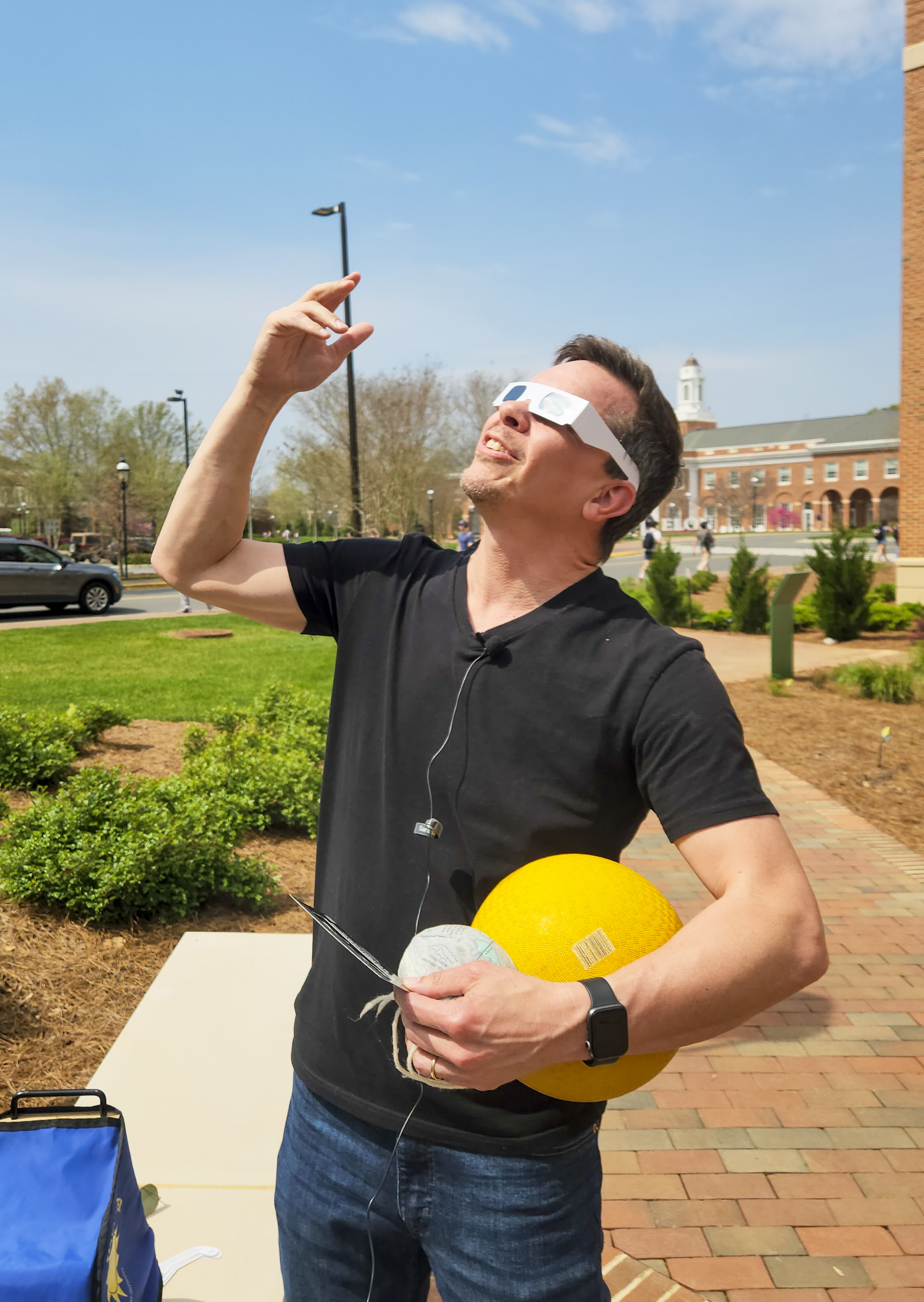 Tony Crider wearing eclipse glasses, holding yellow and white balls, pointing skyward