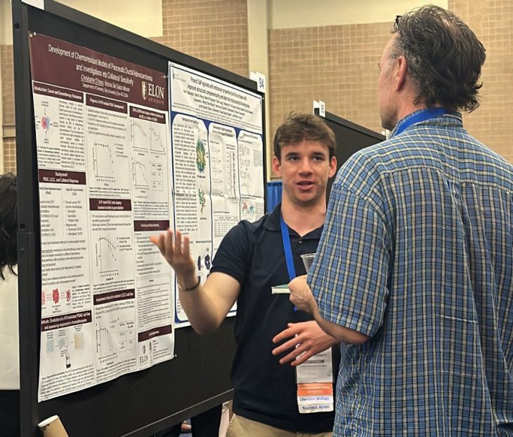 A male student discusses a research poster with an observer