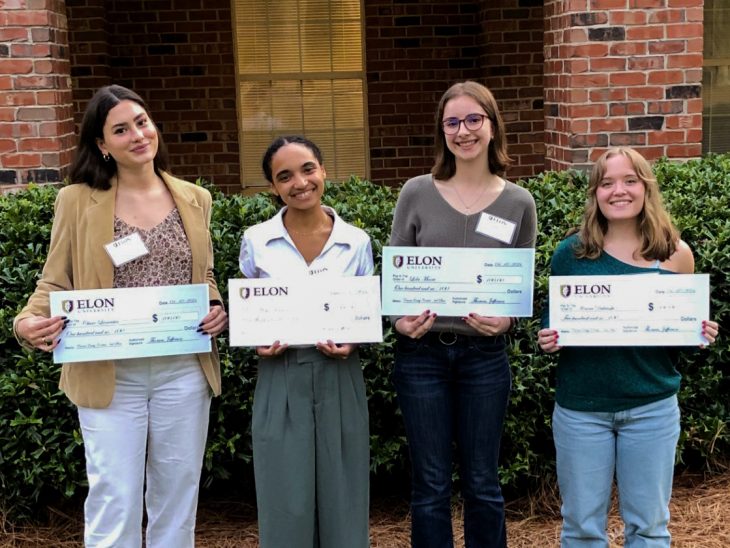 Four female undergraduates holding large checks
