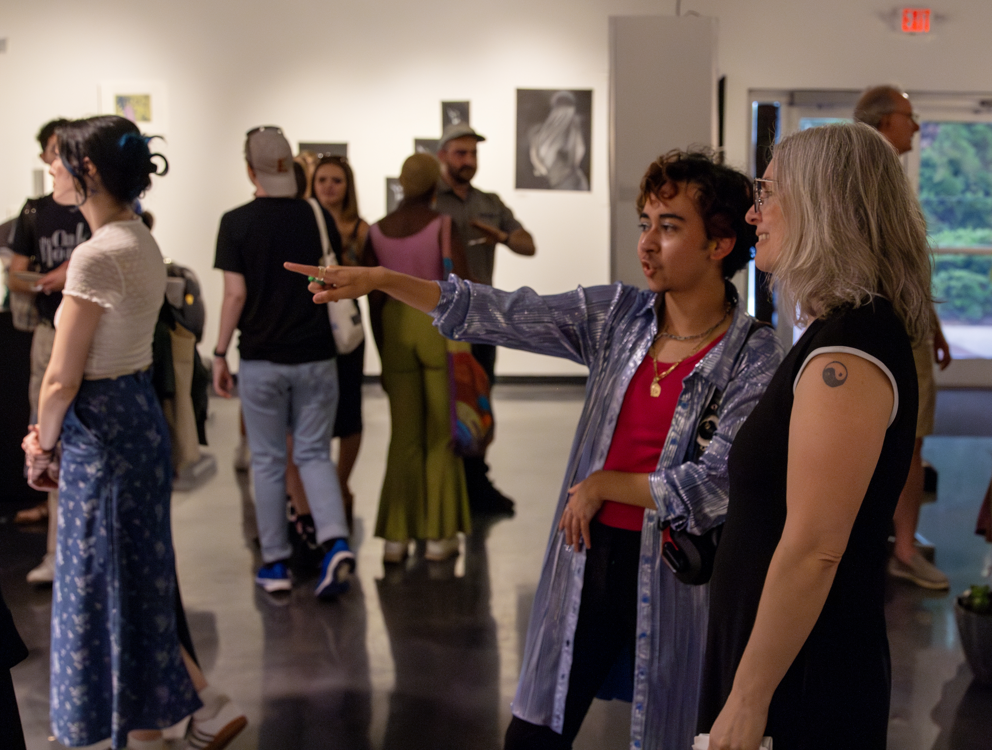 Two people point at and discuss art in a crowded gallery