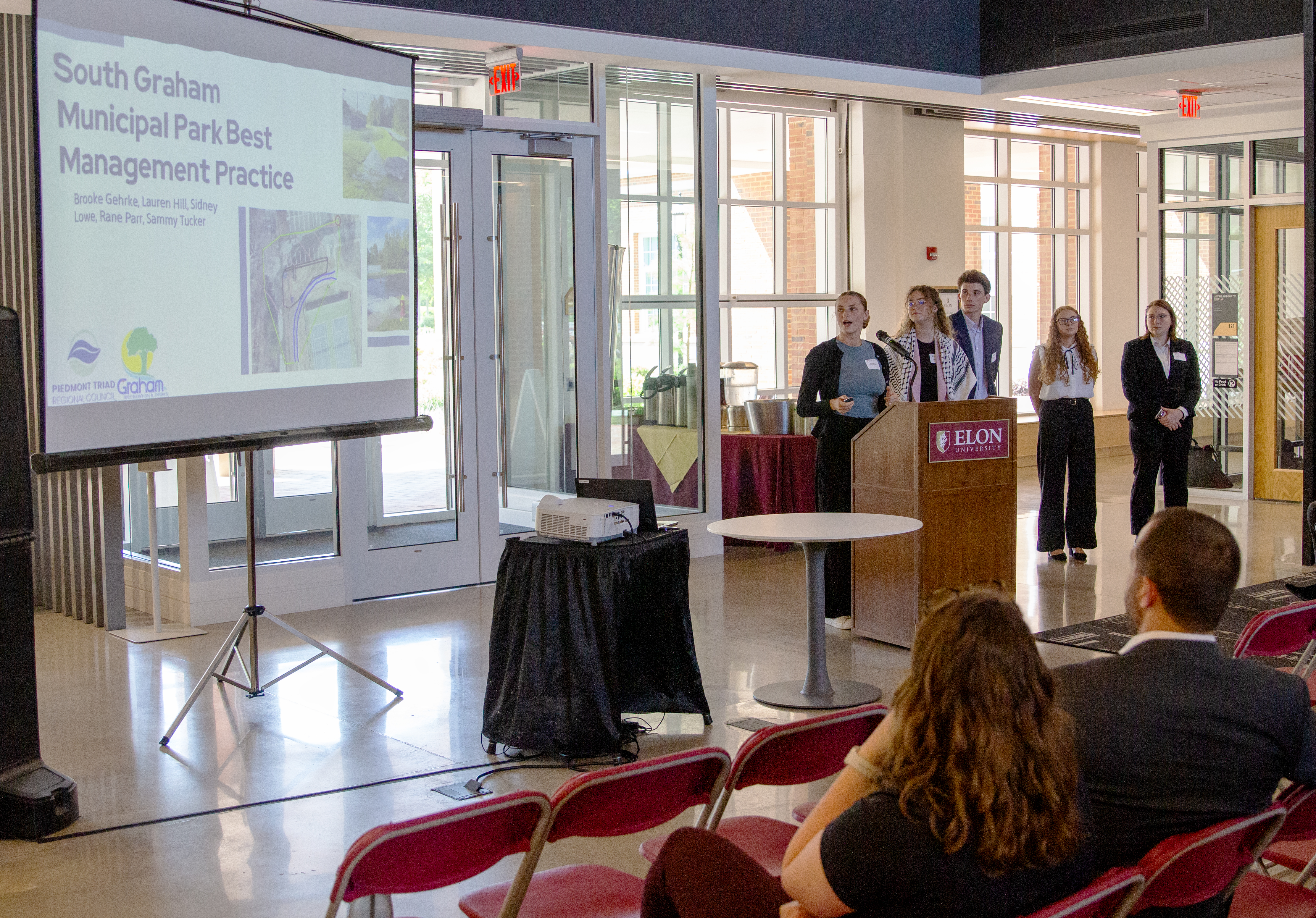 Five students behind a podium in Hunt Atrium in Founders Hall