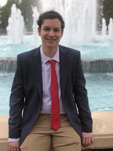 Charlie De Poortere ’24 sits in front of a fountain at Elon University.