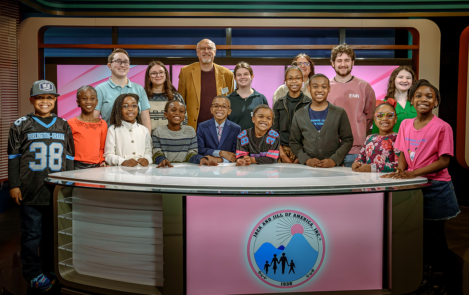 A group of Elon students and Alamance County youth pose behind the Elon studio desk.