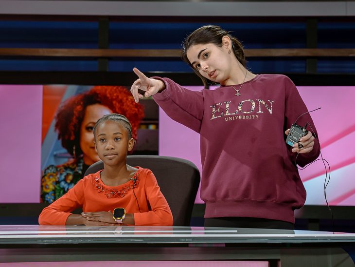 Abby Gravely points while standing behind the Elon anchor desk.