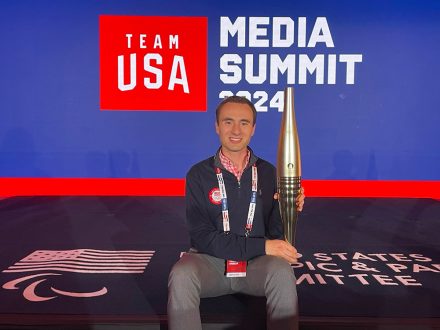 Zach Hrinuk sits in front of a Team USA sign.