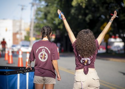 Two Move-In Day volunteers stand together with a blue bin. One person has their arms raised.