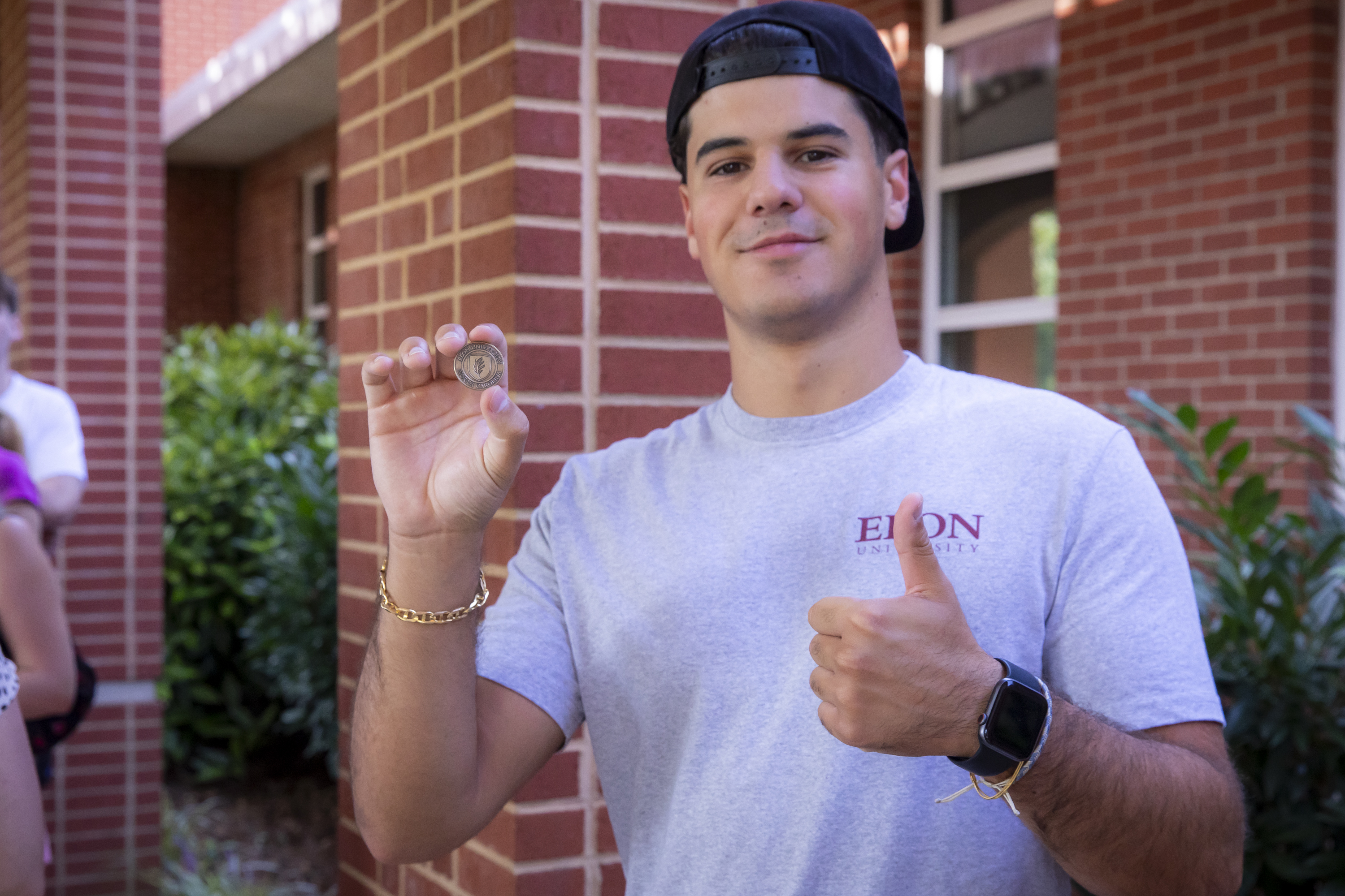 Student holds up honorary coin and shows thumbs up