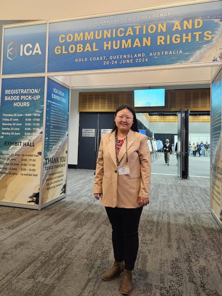 Elon's Chris Chen stands in front of signage for the 74th Annual International Communication Association (ICA) Conference.