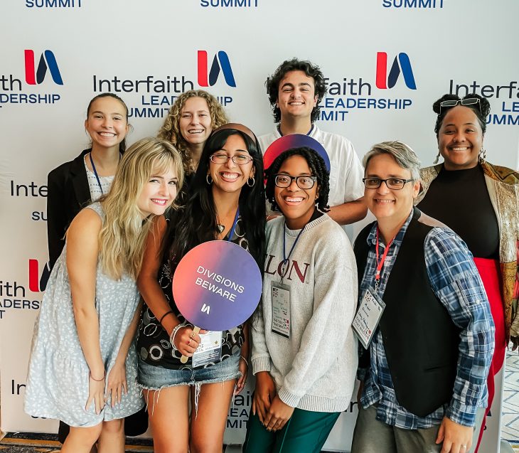 Eight people pose in front of a background with the words "Interfaith Leadership Summit."