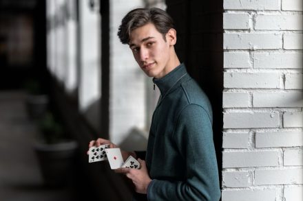 Blair Berenson leans against a wall shuffling cards