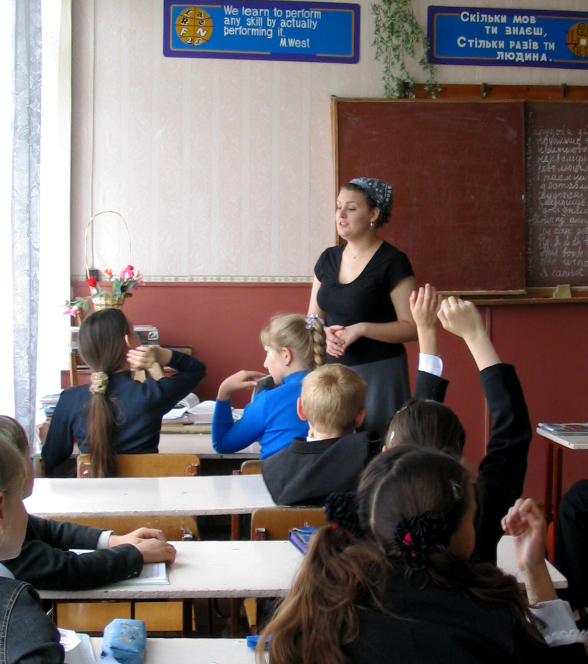 A classroom of students raising their hands as a female teacher asks questions