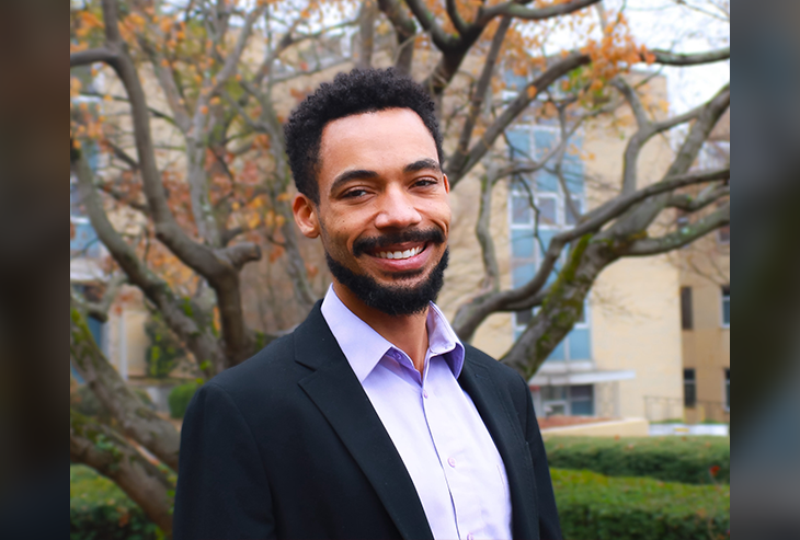 Portrait of Tayo Sanders in blazer and collared shirt on a campus