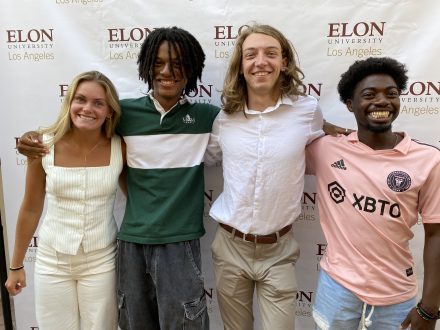 Four students pose for a photo in front of an Elon back drop