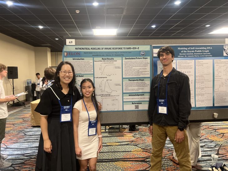 Two students and a professor in front of a research poster in large hall