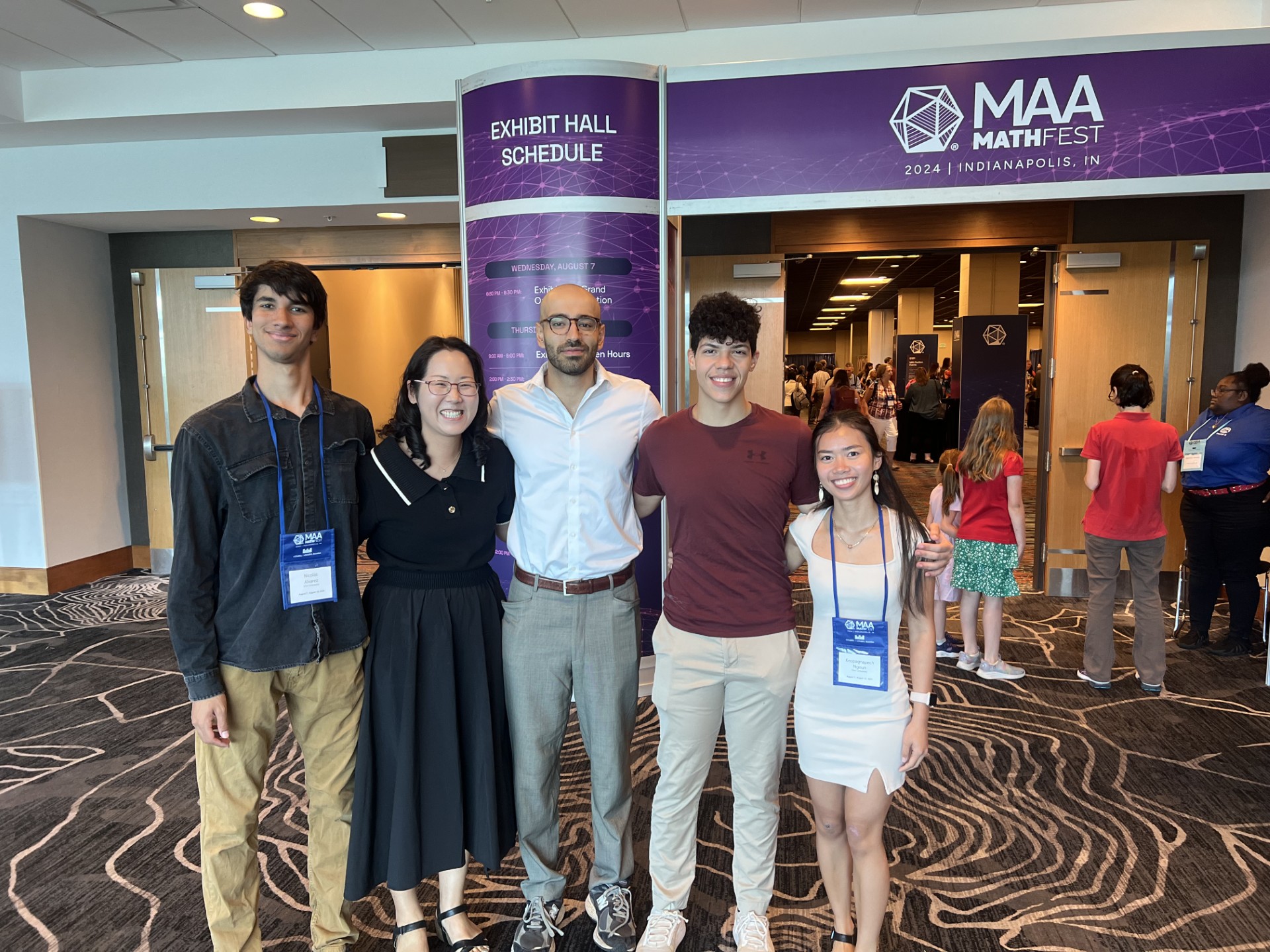 A group of students with a professor in front of a purple MAA banner