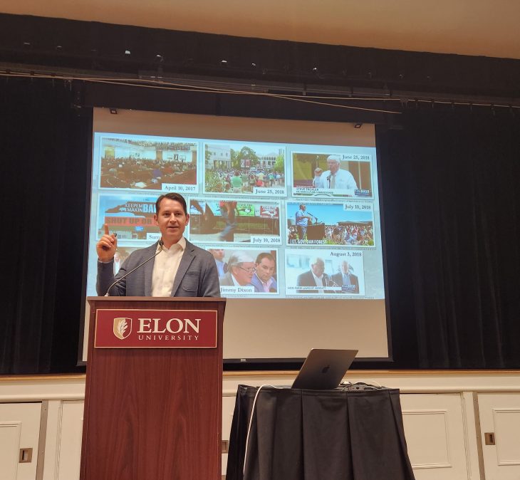 Corban Addison at an Elon podium in front of a projected screen of images