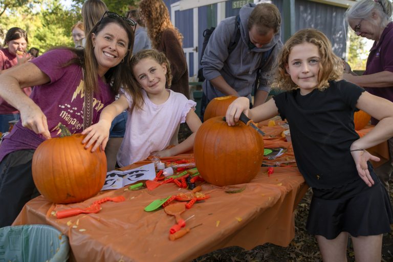 A person and two kids carve pumpkins