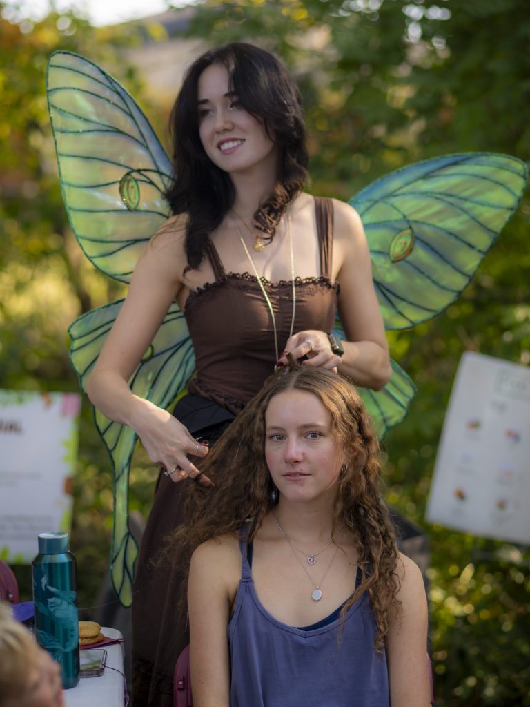 Person in fairy wings holds hair of another person