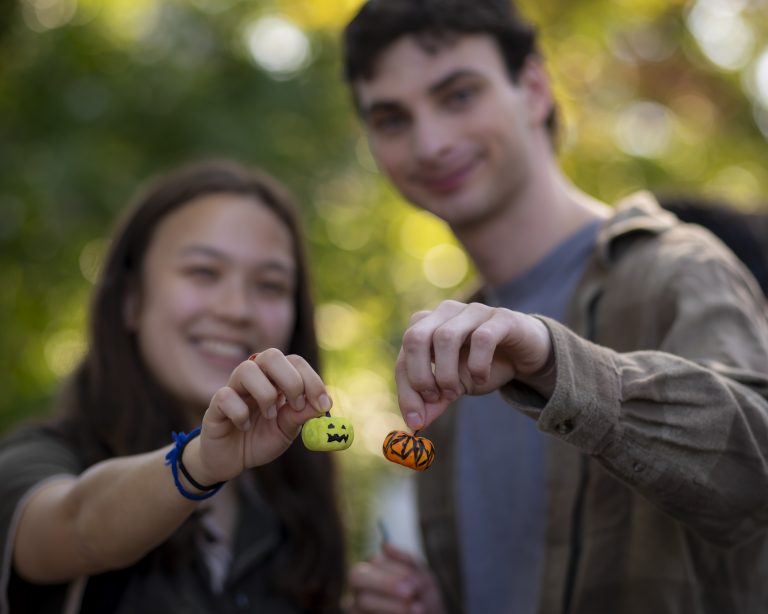 Two people hold up small pumpkins