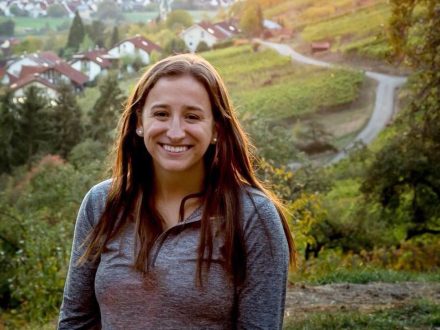 A woman in a sweater stands on a mountainside overlooking a German village.