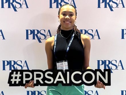 Elon student Evelyn Ealey stands with #PRSAICON sign.