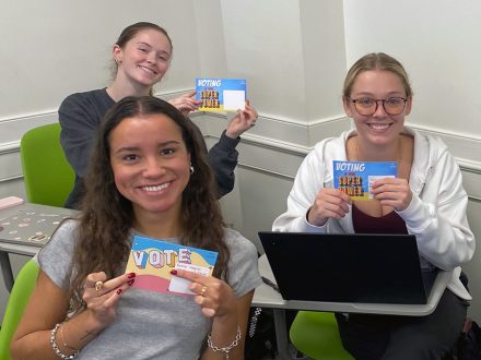 Elon students hold up Get Out to Vote postcards.