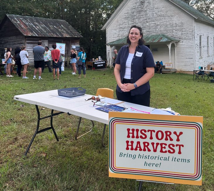 Emily Moser in front of an old meeeting building with a sign that says History Harvest