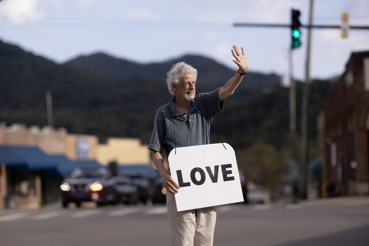 Person holds a sign that reads 'Love' in front of mountains